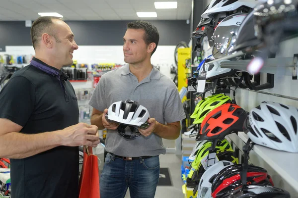 Чоловік вибирає шолом для їзди на велосипеді перед покупкою в спортивному магазині — стокове фото
