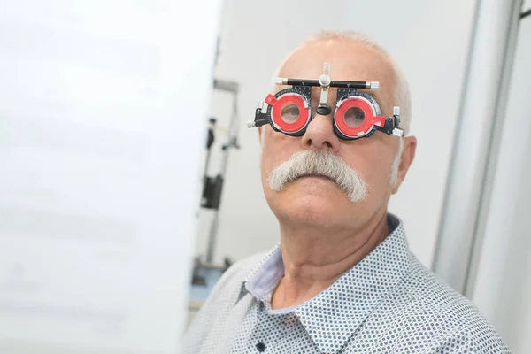 Hombre mayor que usa gafas de prueba ópticas con lentes intercambiables — Foto de Stock