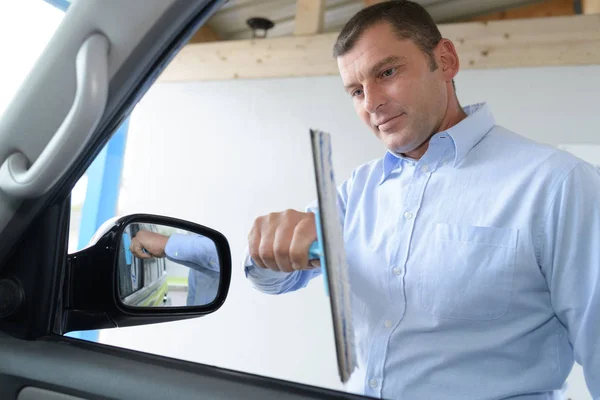 Jovem limpando cuidadosamente suas janelas do carro — Fotografia de Stock