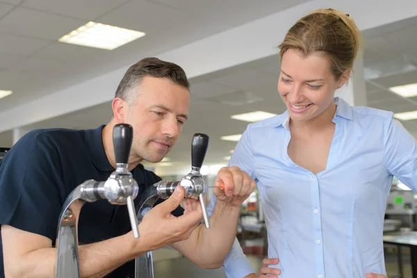 Mature repairman fixing draught beer system with client — Stock Photo, Image