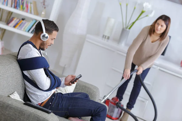 Woman cleaning up while husband is relaxing on the sofa — Stock Photo, Image