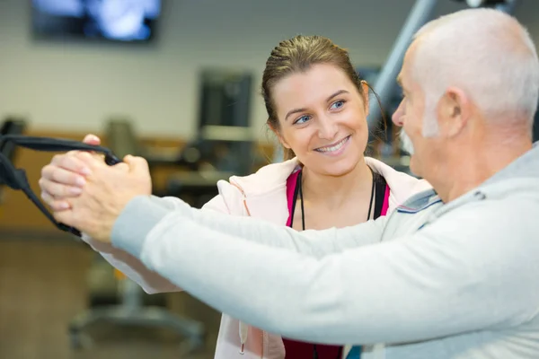 Glad tränare bistå senior man att träna i gymmet — Stockfoto