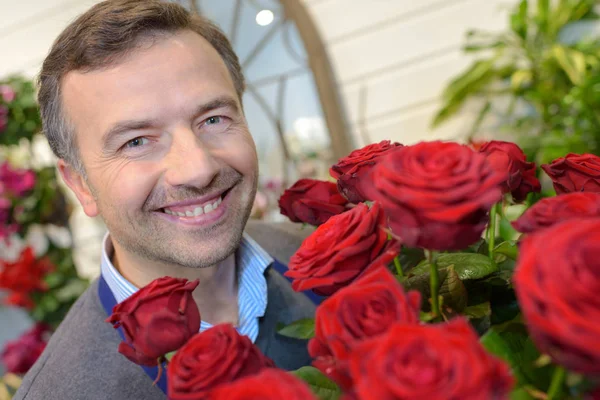 Lyckligt leende florist mannen med röda rosor på blomsteraffär — Stockfoto