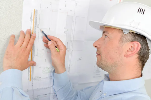 Architect holding plans up to the wall — Stock Photo, Image