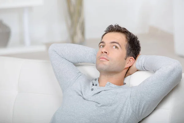 Happy young man relaxing in sofa with arms behind head — Stock Photo, Image