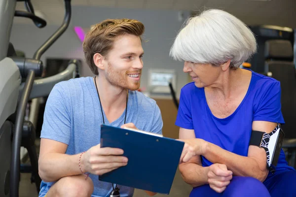 Female senior discussing with a gym trainer looking at clipboard — Stock Photo, Image