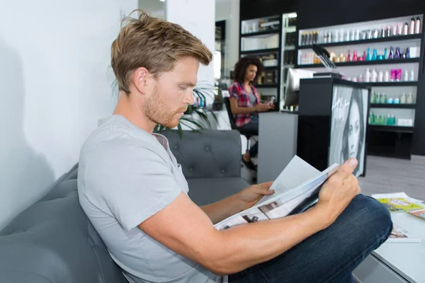 Young man waiting in reception room reading magazine — Stock Photo, Image