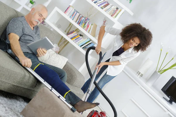 Senior mannen avkopplande medan unga kvinnan städa huset — Stockfoto