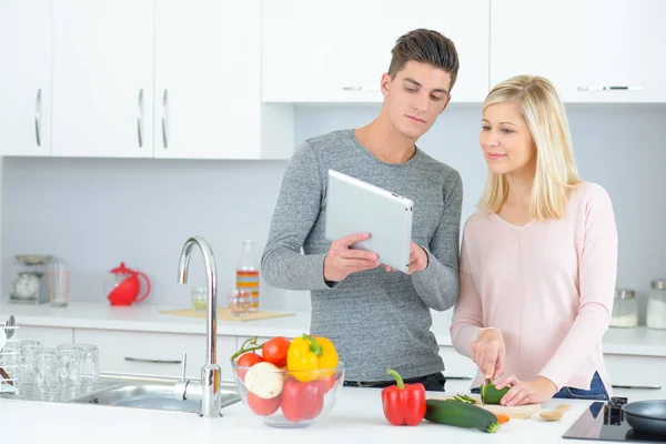 Pareja joven en una cocina mirando la tableta — Foto de Stock