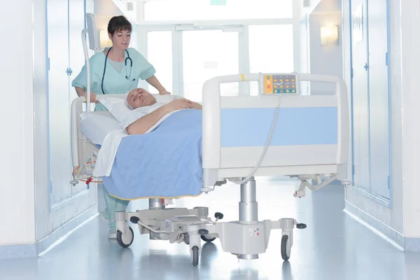 Pielęgniarka pchania łóżku pacjenta korytarza — Zdjęcie stockowe
