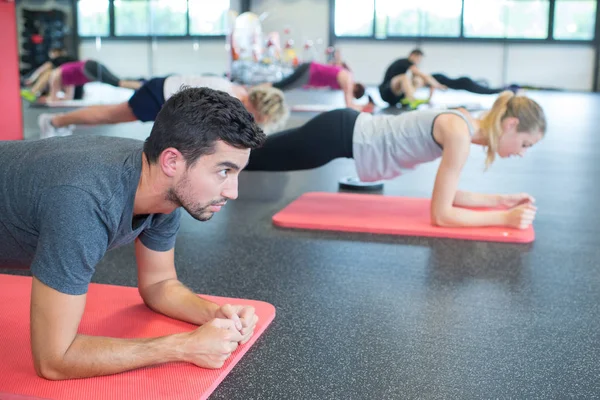 Hombres y mujeres en forma haciendo flexiones en el gimnasio —  Fotos de Stock