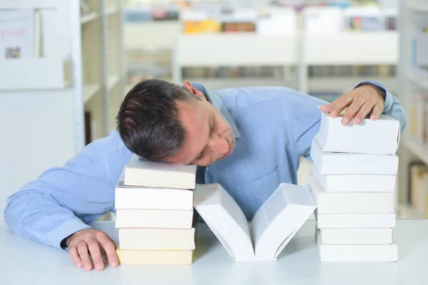 Homem cansado dormindo em uma pilha de livros — Fotografia de Stock