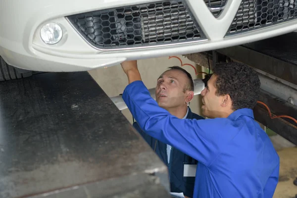 Mecánico y masculino aprendiz trabajando debajo del coche juntos — Foto de Stock