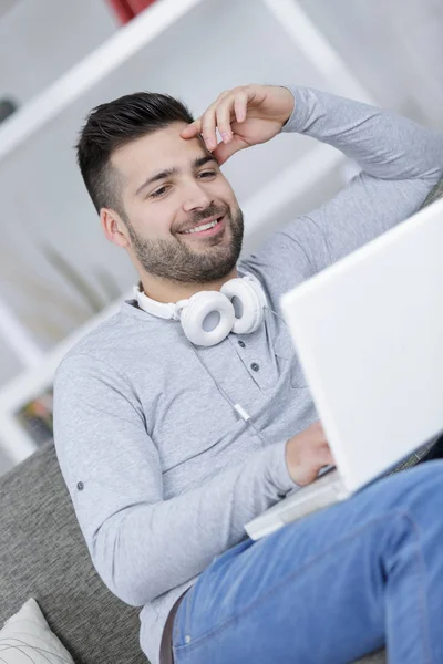 Homem olhando para laptop, fones de ouvido em torno de seu pescoço — Fotografia de Stock