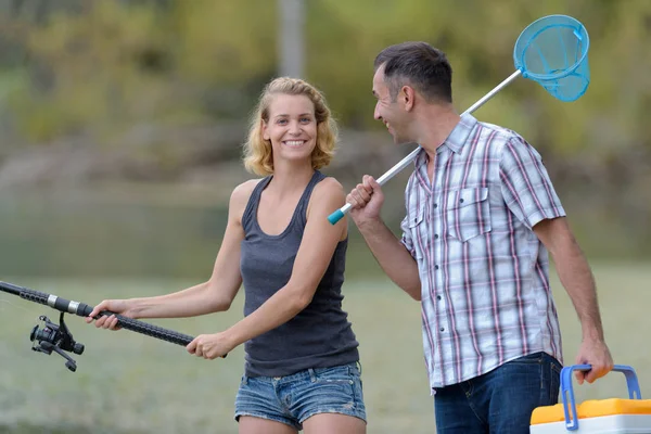 Pareja de pesca o pesca de caña de pie en la orilla del río en la hierba —  Fotos de Stock