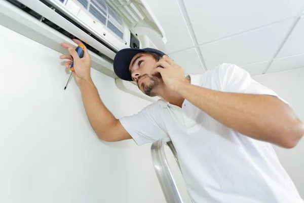 Joven manitas reparando el sistema de aire acondicionado pidiendo ayuda —  Fotos de Stock