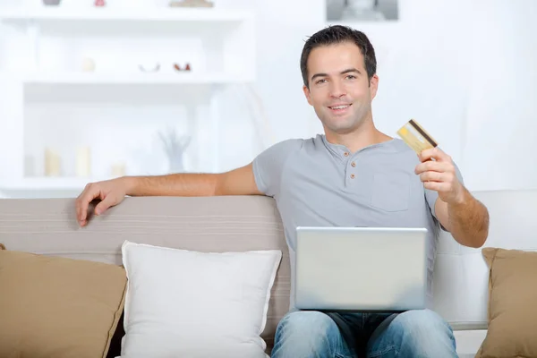 Człowiek na kanapie w domu trzymając laptop i karty — Zdjęcie stockowe
