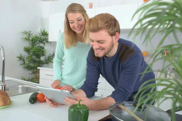 Joven pareja en la cocina seguir una receta de la tableta — Foto de Stock