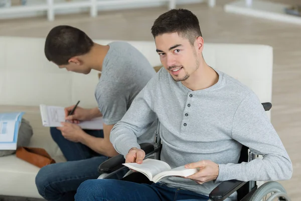 Étudiant masculin en fauteuil roulant avec un ami allant sur leurs devoirs — Photo