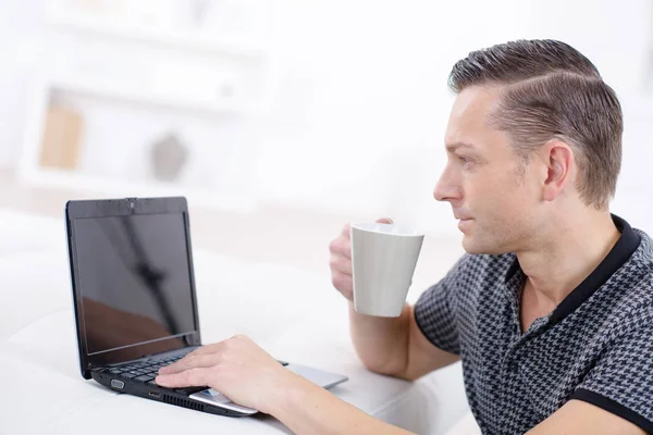 Homem na frente do laptop bebendo em um copo — Fotografia de Stock