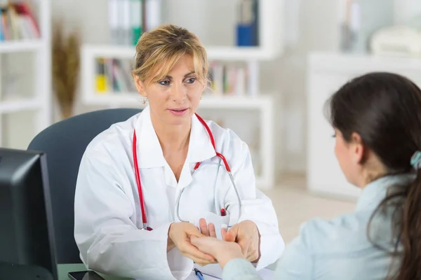 Amigable médico femenino celebrar paciente de la mano en el consultorio durante la consulta —  Fotos de Stock