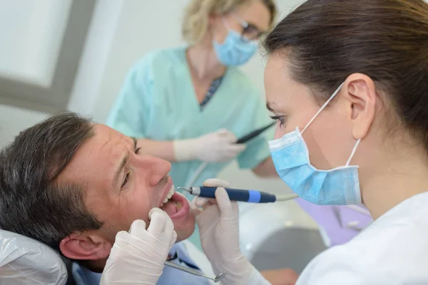 Dentista femenino con asistente y paciente varón asustado —  Fotos de Stock