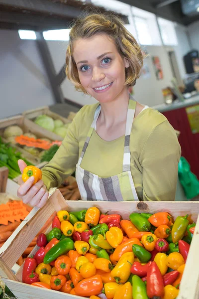 Gärna kvinnliga säljaren poserar med en låda full av paprika — Stockfoto