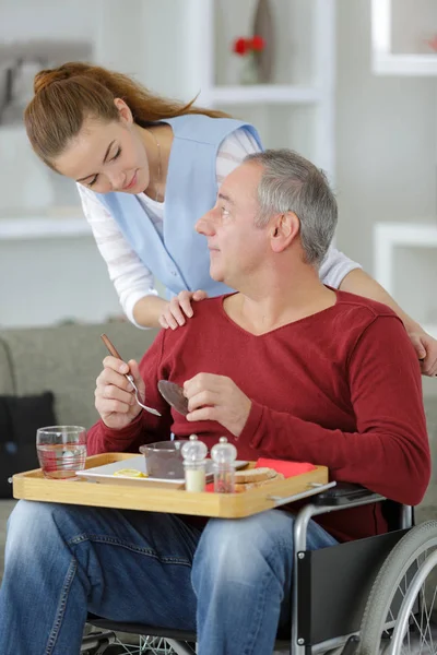 Pflegerin serviert Mann im Rollstuhl zu Hause Mahlzeit — Stockfoto