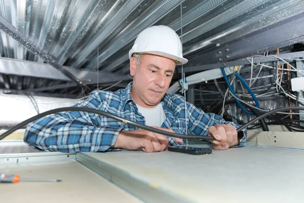 Eletricista segurando cabo no teto de fiação — Fotografia de Stock