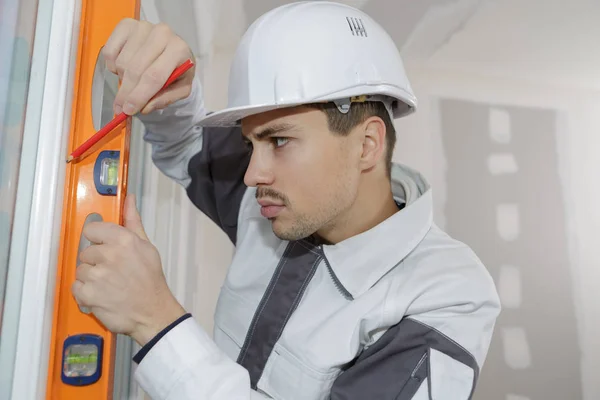 Trabalhador de instrução verificando o nível na parede dentro de casa — Fotografia de Stock