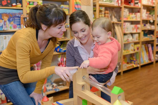 Mutter und Tochter mit attraktivem Verkäufer im Spielwarengeschäft — Stockfoto