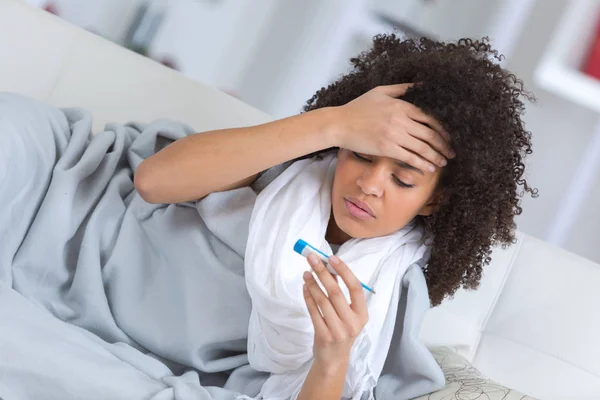 Молода приваблива жінка лежить хвора вдома диван з термометром — стокове фото