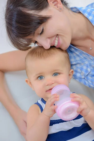 Mother cuddling baby chewing bottle — Stock Photo, Image