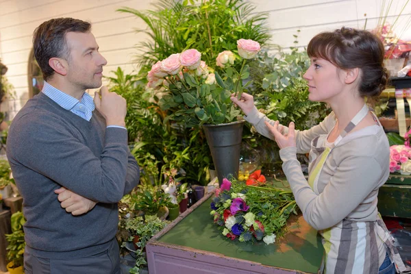 Lachende vrouw verkoper biedt bloemen man — Stockfoto