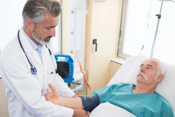 Male doctor examining senior man in hospital — Stock Photo, Image