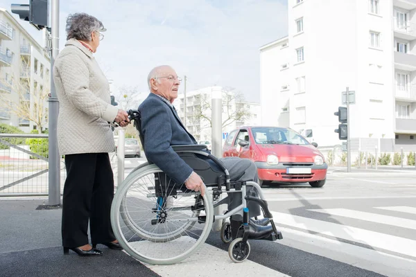 Frau und ältere Person im Rollstuhl überqueren die Straße — Stockfoto