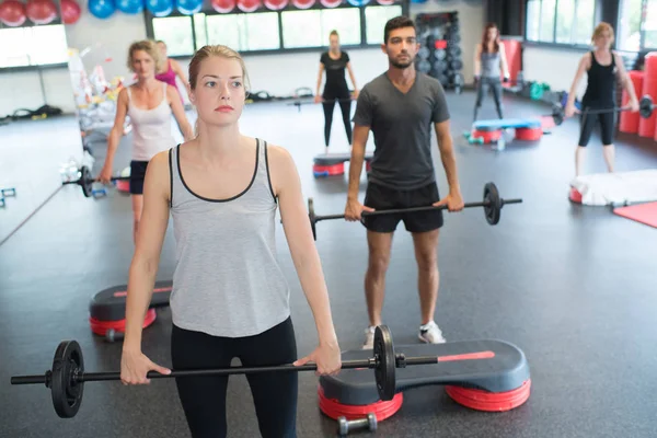 Groupe de personnes faisant de l'exercice avec des barres d'haltères dans la salle de gym — Photo