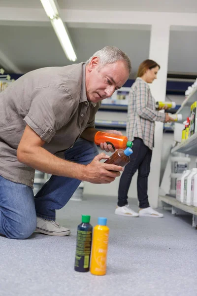 Uomo che sceglie prodotti chimici per la casa nel supermercato — Foto Stock