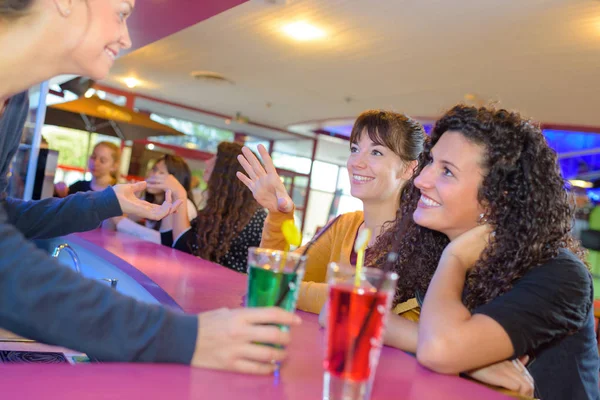 Two female drinking at counter and chatting with bartenders — Stock Photo, Image