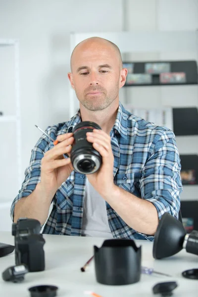 Αρσενικό φωτογράφος συγκόλληση φακό στο χώρο εργασίας του — Φωτογραφία Αρχείου