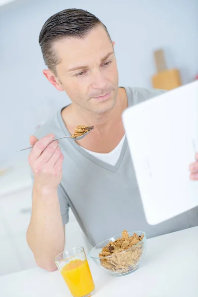 Junger Mann frühstückt mit digitalem Tablet — Stockfoto