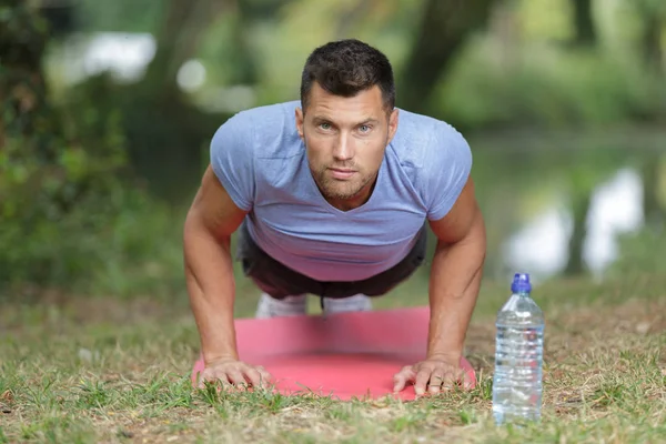 Man doing plank on grass in summer park — Stock Photo, Image