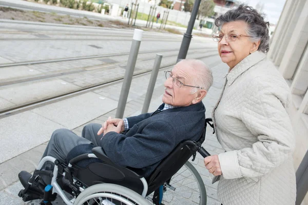 Старшая женщина толкает мужа в инвалидной коляске на перекрёсток — стоковое фото