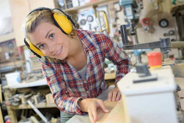 Vrouwelijke timmerman in veiligheid apparatuur snijden hout in werkplaats — Stockfoto