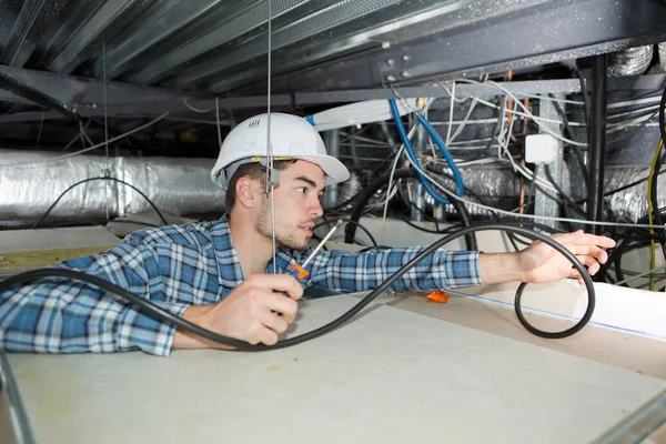 Eletricista masculino com chave de fenda fiação no teto do edifício — Fotografia de Stock