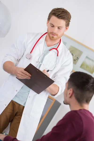 Doctor filling out form with young male patient — Stock Photo, Image