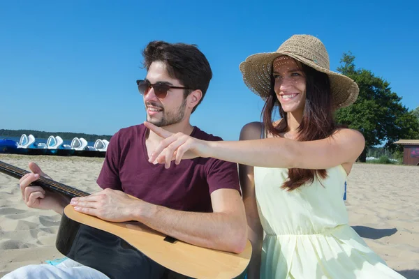 Młody człowiek ze swoją gitarą i dziewczyną na plaży — Zdjęcie stockowe