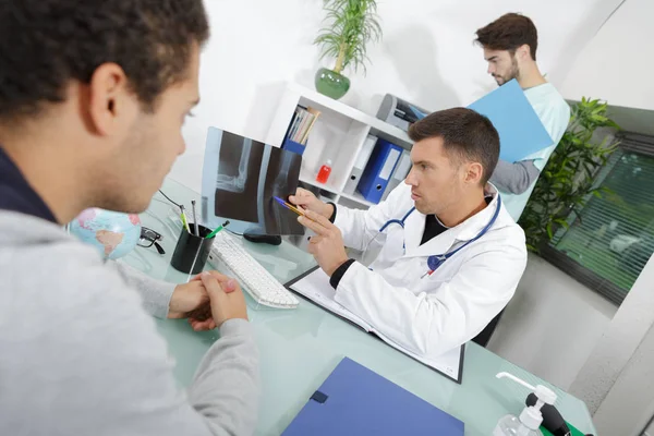 Csinos orvos beszél a férfi beteg, valamint bemutatja a röntgen — Stock Fotó