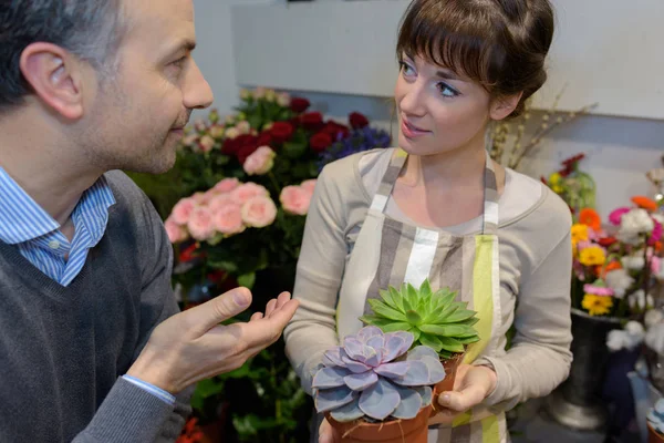 Lachende vrouw verkoper aanbieden bloemen mannelijke client — Stockfoto