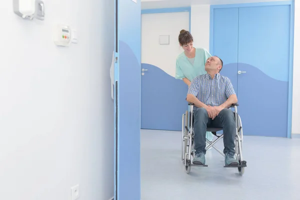 Disabile uomo in sedia a rotelle e infermiera lo sta spingendo — Foto Stock